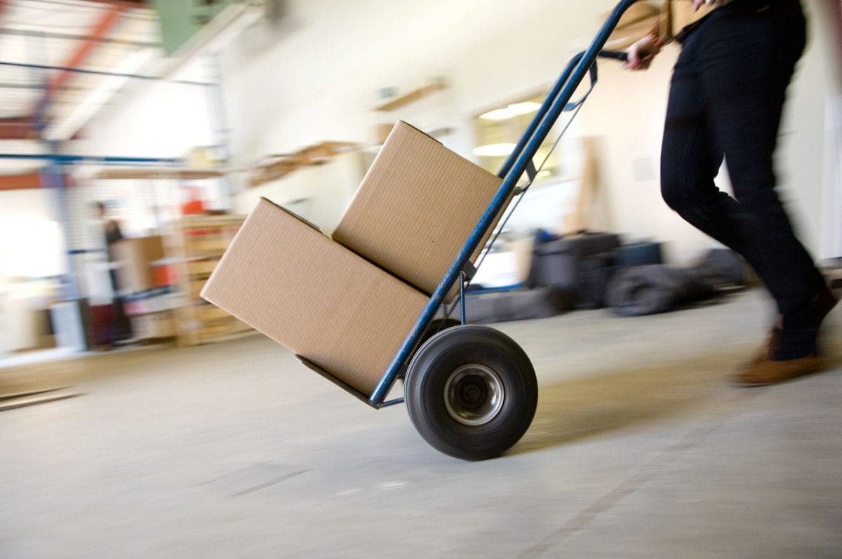 Worker moving cartons on a hand truck across a warehouse floor