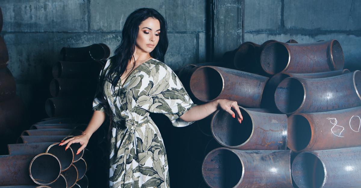 model business concept, factory floor, building materials, beautiful brunette with bright red manicure, in dress and shoes posing among metal pipes.