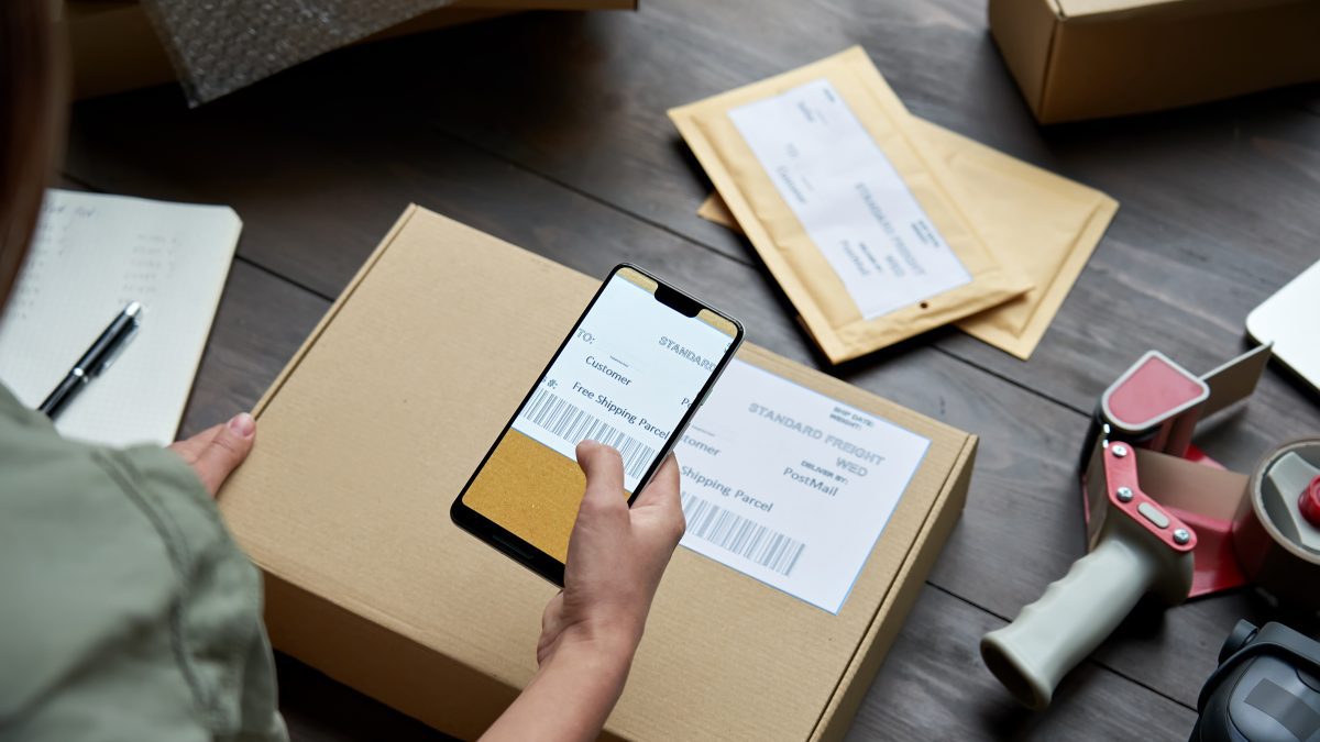female warehouse worker scanning barcode on shipping box on smartphone.