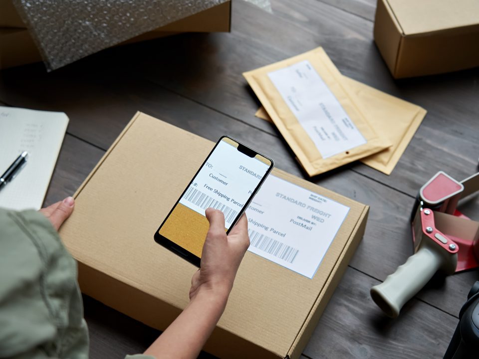 female warehouse worker scanning barcode on shipping box on smartphone.