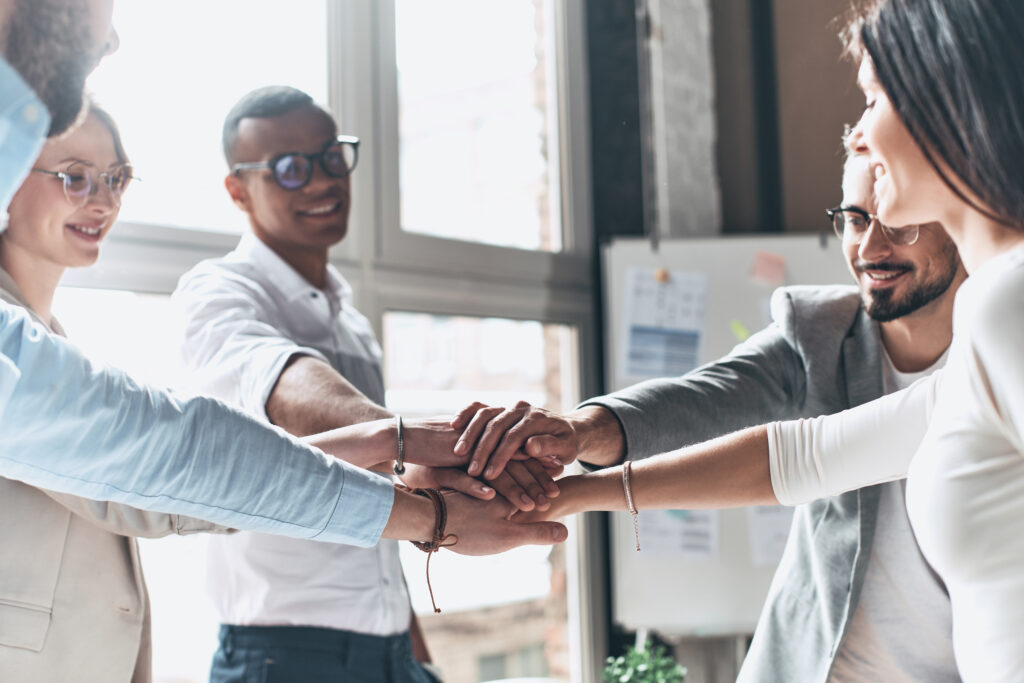 to success! young modern people in smart casual wear holding hands on top of one another in a symbol of unity while working in the creative office