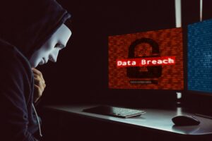 Masked hacker under hood using computer to commit data breach crime
